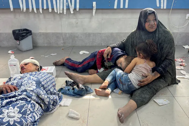 A Palestinian woman holds her children, who were wounded along with her in an Israeli strike, at Shifa hospital in Gaza City on October 23, 2023. (Photo by Mohammed Al-Masri/Reuters)