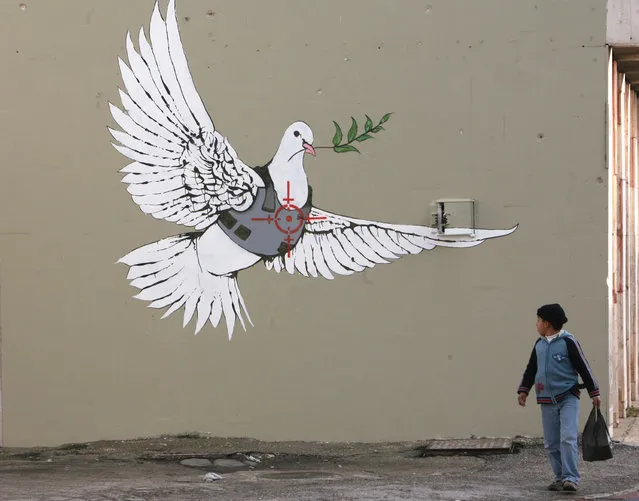 A Palestinian boy looks at an image painted by Banksy as part of a Christmas exhibition in the West Bank town of Bethlehem in 2007. (Photo by Ammar Awad/Reuters)