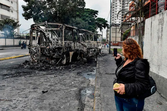 A woman takes a picture of a burned bus, that was set up on fire in Caracas on the eve of a march called by Venezuelan opposition on the anniversary of 1958 uprising that overthrew military dictatorship, on January 23, 2019. At least four people have died following overnight clashes ahead of Wednesday's rival protests in Venezuela by supporters and opponents of President Nicolas Maduro, two days after a failed mutiny by soldiers hoping to spark a movement that would overthrow Maduro, police and non-governmental organizations said. (Photo by Luis Robayo/AFP Photo)