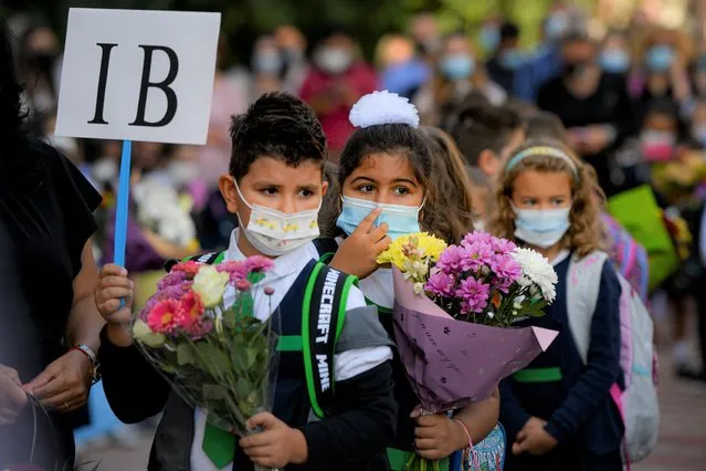 Children wearing face masks hold flowers during festivities marking the beginning of the school year at a school in Bucharest, Romania, Monday, September 13, 2021. Children returned to classrooms in Romania, a country with one of the lowest COVID-19 vaccination rates in the European Union, as the daily infection numbers continue to rise. (Photo by Andreea Alexandru/AP Photo)