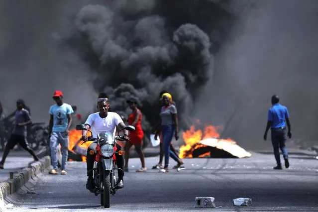 A man drives past a burning barricade during a protest against Prime Minister Ariel Henry's government and insecurity, in Port-au-Prince, Haiti on March 1, 2024. (Photo by Ralph Tedy Erol/Reuters)