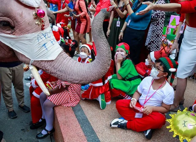 Students receive gifts from an elephant during a the visit of five elephants in Santa Claus costumes with giant face masks delivering hand sanitizers and promoting a “get vaccinated” message at a primary school, in the historical city of Ayutthaya, Thailand, December 24, 2021. (Photo by Soe Zeya Tun/Reuters)