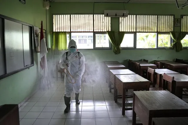 An Indonesian Red Cross worker sprays disinfectant inside an empty classroom at a high school during the suspension of activities after a case of COVID-19 is found at the school, in Jakarta, Indonesia, Friday, January 28, 2022. Dozens of schools in the capital city were temporarily closed following the findings of coronavirus cases among students and staff. (Photo by Dita Alangkara/AP Photo)