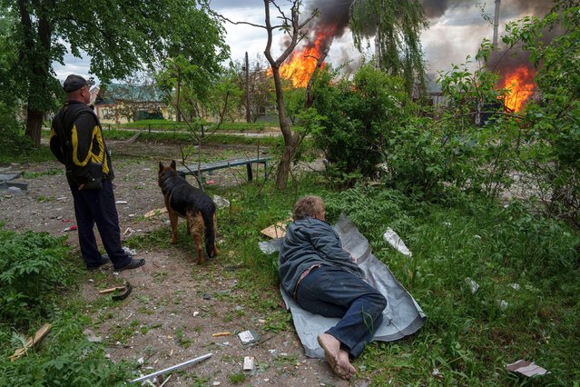 A man lies on the ground as he watches his burning house destroyed by a Russian airstrike in Vovchansk, Ukraine, on Saturday, May 11, 2024. (Photo by Evgeniy Maloletka/AP Photo)