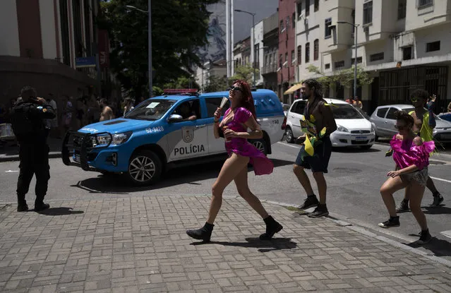 Police patrol an area as revelers cross a street during an unofficial carnival block party referred to as “blocos”, in Rio de Janeiro, Brazil, Saturday, February 26, 2022. (Photo by Silvia Izquierdo/AP Photo)