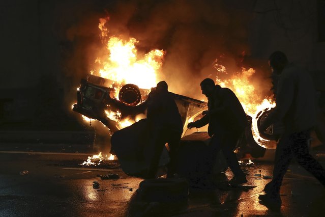 Protesters move a dumpster in front of a burning police car not far from the Georgian parliament building in Tbilisi, Georgia, Thursday, March 9, 2023. Police in Georgia's capital have fired water cannon and tear-gas to disperse demonstrators around the parliament building protesting a draft law aimed at curbing the influence of “foreign agents”, among fears it could be used to silence oppositions. (Photo by Zurab Tsertsvadze/AP Photo)