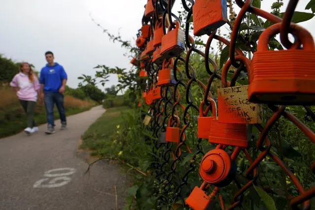 A couple walks past a lock left on a fence along the Cliff Walk in Newport, Rhode Island July 14, 2015. (Photo by Brian Snyder/Reuters)