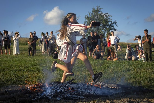 A young woman takes selfie as she jumps over the fire at a traditional Midsummer Night celebration near capital Kyiv, Ukraine, Sunday, June 23, 2024. The age-old pagan festival is still celebrated in Ukraine amid the third year of Russia-Ukraine war. Many people believe that jumping over the fire will cleanse them of evil spirits. (Photo by Efrem Lukatsky/AP Photo)