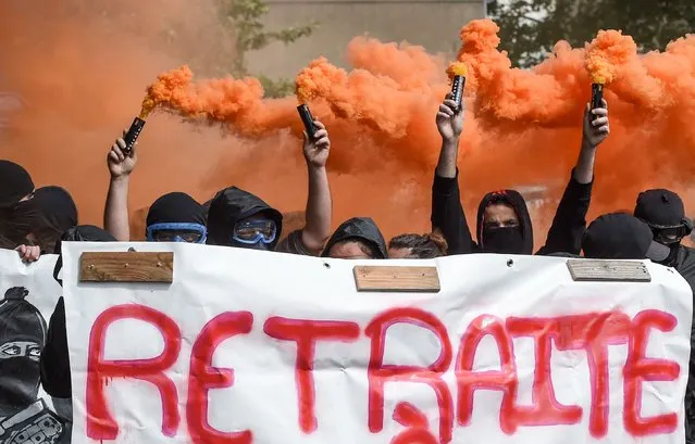 Protestors hold smoke bombs and a banner reading “retirement at 20” as they take part in the traditional May Day rally in Nantes, western France, on May 1, 2022. (Photo by Sebastien Salom-Gomis/AFP Photo)