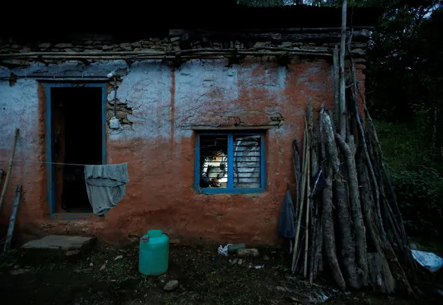 Durga Kami, 68, who is studying in the tenth grade at Shree Kala Bhairab Higher Secondary School, is seen through the window as he prepares dinner for himself at his one room house in Syangja, Nepal, June 4, 2016. (Photo by Navesh Chitrakar/Reuters)