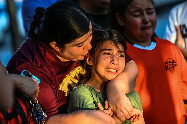 Gabriella Uriegas, a soccer teammate of Tess Mata who died in the shooting, cries while holding her mother Geneva Uriegas as they visit a makeshift memorial outside the Uvalde County Courthouse in Texas on May 26, 2022. Texas police faced angry questions May 26, 2022 over why it took an hour to neutralize the gunman who murdered 19 small children and two teachers in Uvalde, as video emerged of desperate parents begging officers to storm the school. (Photo by Chandan Khanna/AFP Photo)