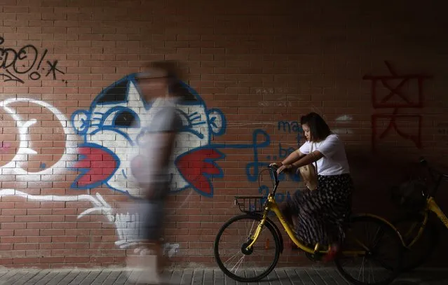 A visitor walks past graffiti art as a cyclist waits by at 798 Art district in Beijing, China, 26 August 2017. The Beijing 798 art district is made up of a complex of decommissioned military factory buildings, housing a variety of quirky art galleries and cafes popular with tourists and young people. (Photo by How Hwee Young/EPA/EFE)