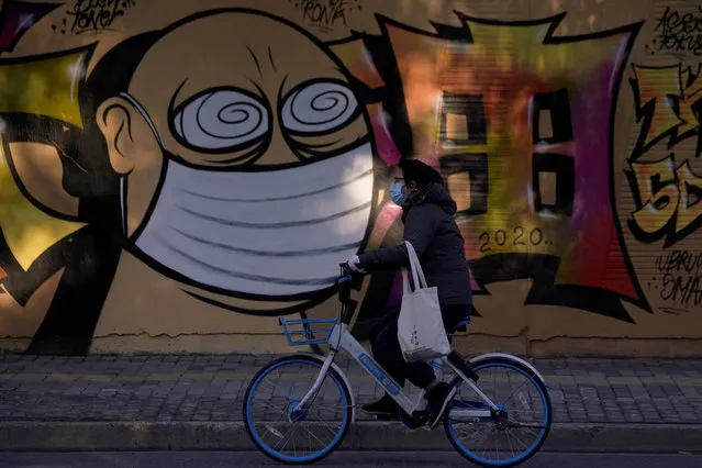 A woman wearing a protective mask cycles past graffiti-painted wall at a construction site in Shanghai, China, as the country is hit by coronavirus outbreak, February 17, 2020. (Photo by Aly Song/Reuters)