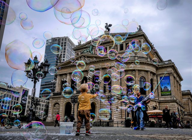 A boy plays with bubbles made by a soap bubble artist in front of the Old Opera in Frankfurt, Germany, Tuesday, August 17, 2021. (Photo by Michael Probst/AP Photo)