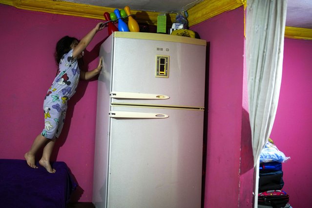 Dilan Sahin stands on a sofa back to obtain a toy that was out of reach, in her family's one-room apartment in the Tarlabasi neighborhood in Istanbul, Turkey, December 4, 2024. (Photo by Francisco Seco/AP Photo)