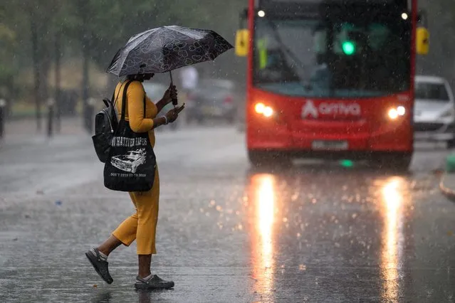 A woman uses an umbrella for shelter as she crosses the road, as torrential rain and thunderstorms hit the country on August 17, 2022 in London, England. After the UK experienced a second summer heatwave, storms are expected starting in the north of the country from Monday moving to the whole country by Wednesday, with flood alerts issued by the Met Office. (Photo by Leon Neal/Getty Images)