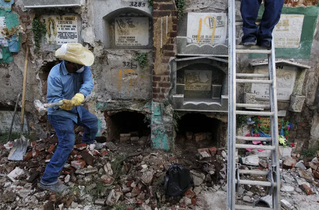 A grave cleaner uses a maul to break the cover of a crypt as a fellow grave cleaner works standing on a ladder during exhumation works at the Cemetery General in Guatemala City January 29, 2014. Any remains that have not been claimed are packed into plastic bags, labeled and stored in mass graves. (Photo by Jorge Dan Lopez/Reuters)