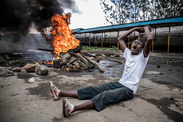 An opposition supporter reacts under the heavy rain in front of a burning barricade in Mathare district, in Nairobi on October 26, 2017, as a group of demonstrators blocked the road and tried to prevent voters from accessing a polling station during presidential elections. (Photo by Luis Tato/AFP Photo)