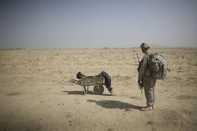 A US Army soldier from Scout Platoon 502 Infantry Regiment, 101st Airborne Division, looks at the body of a suspected Taliban IED emplacer who was killed in a coalition missile strike in Zhari district, Kandahar province, Sunday, October 10, 2010. The Scouts' mission was to support roadside bomb clearance efforts in the militant stronghold, the latest days-long phase of Operation Dragon Strike. (Photo by Rodrigo Abd/AP Photo)