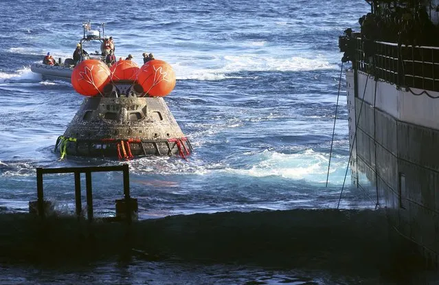 NASA's Orion Capsule is drawn to the well deck of the USS Portland during recovery operations after it splashed down in the Pacific Ocean off the coast of Baja California, Mexico, on December 11, 2022. Orion was launched November 16 on the Artemis rocket for a 25-day mission to the Moon. The main goal of this mission was to test Orion's heat shield – for the day when it is humans and not test mannequins riding inside. (Photo by Mario Tama/Pool via AFP Photo)
