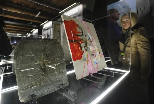 A visitor looks at artworks made from used armor plates from bulletproof vests of Ukrainian soldiers during the “ArtArmor” exhibition in the Western Ukrainian city of Lviv, 27 December 2022. A group of Ukrainian artists created 12 art objects from used armor plates that have already successfully fulfilled their mission in battle – stopping enemy bullets and shrapnel on a front line. The armor plates received a second life in the form of artwork, and their sale will allow volunteers to send money to the Ukrainian army. Russian troops entered Ukraine on 24 February 2022, starting a conflict that has provoked destruction and a humanitarian crisis. (Photo by Mykola Tys/EPA/EFE)