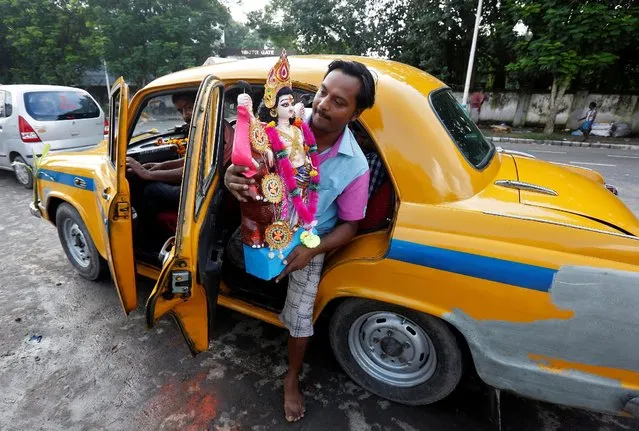 A devotee exits a taxi carrying an idol of Lord Vishwakarma, the Hindu deity of architecture and machinery, to immerse it into the waters of the river Ganga in Kolkata, India, September 19, 2016. (Photo by Rupak De Chowdhuri/Reuters)