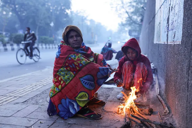 A woman and her daughter warm themselves by a fire on a roadside pavement, on a cold winter morning in New Delhi, India on December 28, 2022. (Photo by Anushree Fadnavis/Reuters)