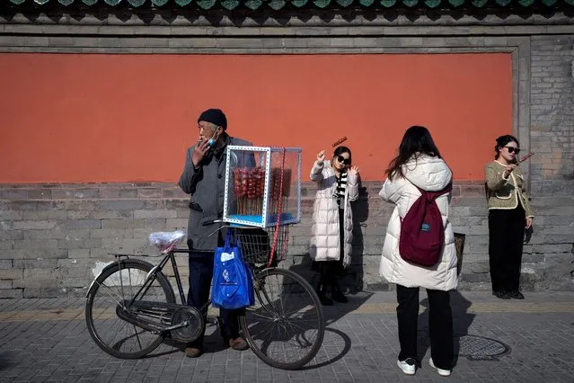 A vendor selling sugar-coated Chinese haws on his bicycle as visitors pose for photos with their purchased sugar-coated haws outside the Drum Tower in Beijing, Monday, January 30, 2023. Chinese people are enjoying the Lunar New Year and visiting various tourist sites in cities around China following the lifting last month of draconian COVID-19 restrictions, allowing a return to many aspects of normal life. (Photo by Andy Wong/AP Photo)