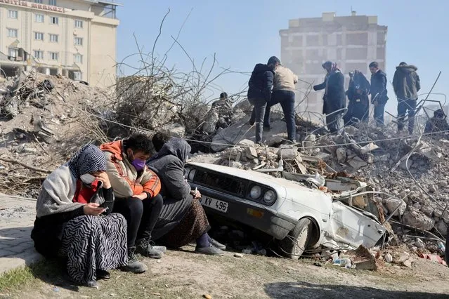 People sit as others search amid the rubble in the aftermath of a deadly earthquake in Kahramanmaras, Turkey on February 14, 2023. (Photo by Nir Elias/Reuters)