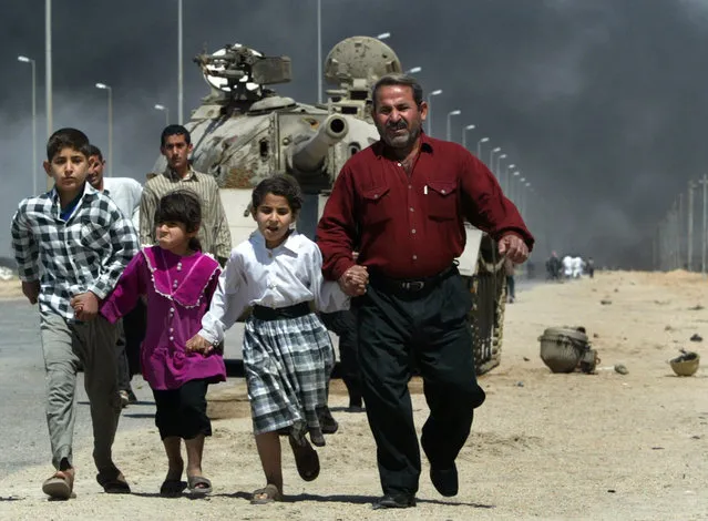 A family flees past a destroyed Iraqi T-55 tank after a mortar attack on British Army positions in the southern city of Basra, March 28, 2003. Iraqi forces fired on about 2,000 civilians trying to flee fighting and a humanitarian crisis in the beseiged southern city of Basra, forcing some to turn back. (Photo by Chris Helgren/Reuters)