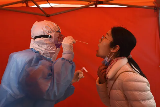 In this photo released by China's Xinhua News Agency, a worker wearing a protective suit takes a throat sample from a woman at a COVID-19 testing site in Tianjin, China, Saturday, November 21, 2020. China is starting mass testing on 3 million people in a section of the northern city of Tianjin and has tested several thousand others in a hospital in Shanghai after the discovery of a pair of cases there. (Photo by Zhao Zishuo/Xinhua via AP Photo)