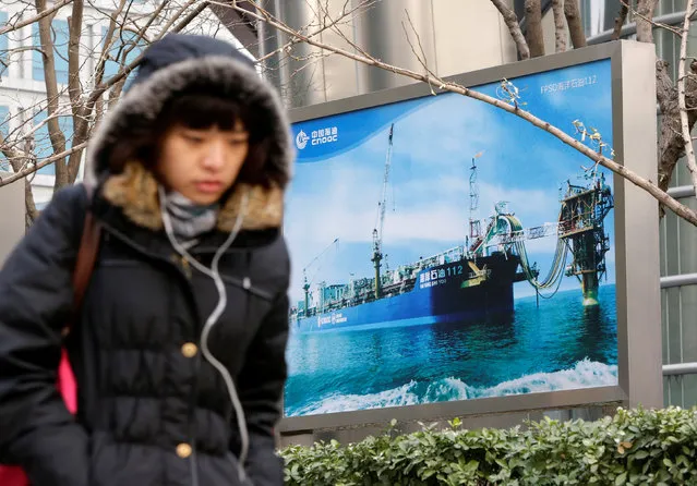 A woman walks past a China National Offshore Oil Corp (CNOOC) poster showing an offshore work platform, next to its headquarters in Beijing, December 10, 2012. (Photo by Jason Lee/Reuters)