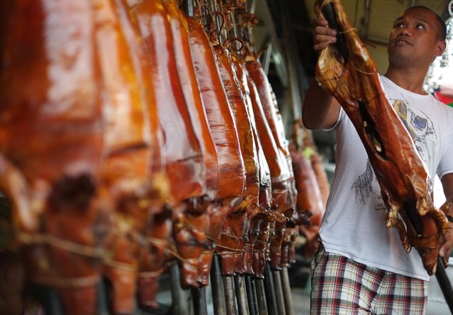 A Filipino worker arranges roasted pigs which they sell in suburban Quezon city, Philippines on Tuesday, December 23, 2014. Roasted pig is popular during Filipino celebrations and traditionally served during a Christmas eve dinner called “Noche Buena” in this predominantly Roman Catholic nation. (Photo by Aaron Favila/AP Photo)