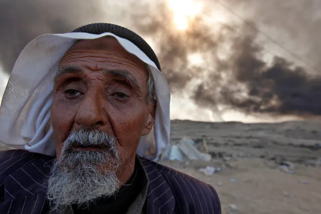 A man returns to his village after it was liberated from Islamic State militants, south of Mosul in Qayyara, Iraq, October 22, 2016. The fumes in the background are from oil wells that were set ablaze by Islamic State militants. (Photo by Alaa Al-Marjani/Reuters)