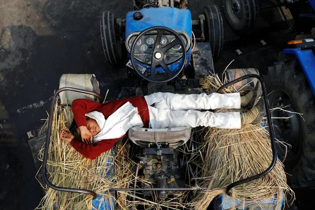 A farmer's son sleeps on a tractor at the site of a protest against new farm laws, at the Delhi-Uttar Pradesh border in Ghaziabad, India, December 23, 2020. (Photo by Adnan Abidi/Reuters)