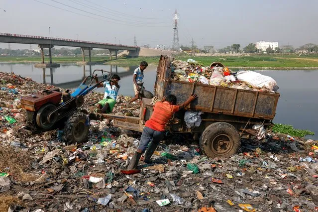 Workers dump waste into a landfill located just beside Dhaleshwari river, water from which flows into the Buriganga river, in Savar, near Dhaka, Bangladesh on March 7, 2023. (Photo by Mohammad Ponir Hossain/Reuters)