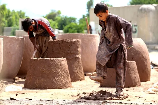 An Afghan boy and man work on clay ovens in Nangarhar province on May 21, 2023. (Photo by Shafiullah Kakar/AFP Photo)