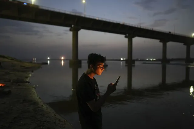 A youth checks his mobile phone standing on the bank of the River Ganges in Prayagraj, India, Wednesday, June 7, 2023. (Photo by Rajesh Kumar Singh/AP Photo)