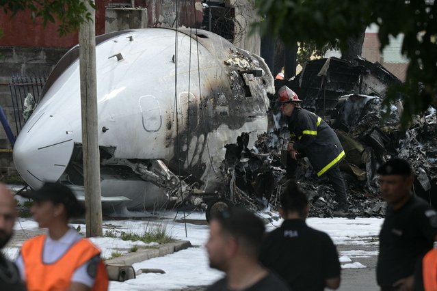 A firefighter inspects the wreckage of a Challenger 300 aircraft that crashed upon landing in the town of San Fernando, Buenos Aires Province, on December 18, 2024. The pilot and co-pilot died after the private plane crashed and caught fire near the airport of San Fernando. The plane was travelling from the exclusive resort of Punta del Este, in Uruguay, and on landing “could not brake”, Carlos Armentano, a spokesman for Aeropuertos Argentina, the company in charge of the airport's operation, told AFP. No other injuries were reported. (Photo by Juan Mabromata/AFP Photo)