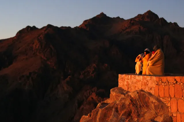 Tourists watch the sunrise and pray outside a church on the summit of Mount Moses, near the city of Saint Catherine, in the Sinai Peninsula, south of Egypt, December 9, 2015. According to the Bible the mountain is where Moses received the ten commandments from God. (Photo by Amr Abdallah Dalsh/Reuters)