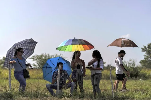 Spectators shade themselves with umbrellas as they wait for the start of drag races at an old, unused airstrip in San Nicolas de Bari, Cuba, Sunday, July 23, 2023. (Photo by Ramon Espinosa/AP Photo)