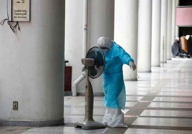 A Thai health official wearing a full protective suit cools down with an electric fan during a free COVID-19 nasal swab test for at-risk people in a bid to curb the rapid spreading of the pandemic in Bangkok, Thailand, 17 April 2021. The Thai government declared Bangkok and other provinces as maximum control areas and tightening strict health measures in a bid to contain the ongoing rapidly rising of infections after the new COVID-19 coronavirus pandemic cases surge to thousands infections daily. (Photo by Rungroj Yongrit/EPA/EFE)