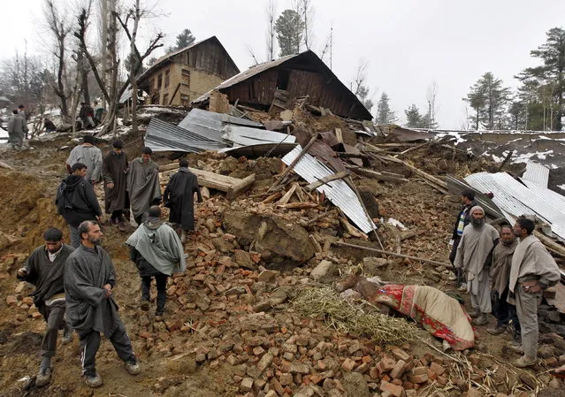 People stand amidst the rubble after a hillside collapsed onto a house at Laden village, west of Srinagar, March 30, 2015. Hundreds of people fled their homes as Kashmir's main rivers began to swell and weather forecasters predicted further downpours in the region that was struck by devastating floods seven months ago. (Photo by Danish Ismail/Reuters)