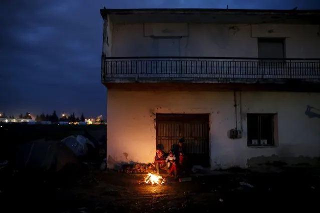 A refugee family gathers around a bonfire next to an abandoned building, near a makeshift camp at the Greek-Macedonian border, near the village of Idomeni, Greece March 16, 2016. (Photo by Alkis Konstantinidis/Reuters)