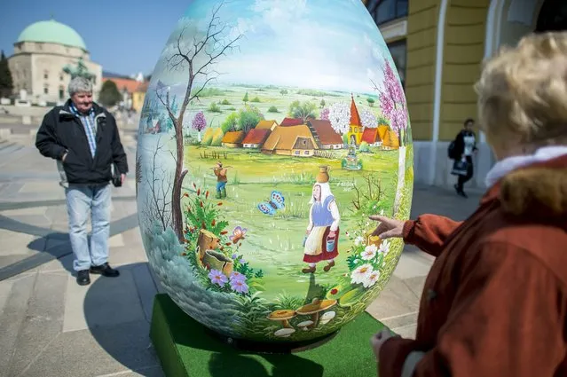 Passers-by look at a giant painted Easter decoration in the shape of an egg on display at Szecheny Square in downtown Pecs, 196 kms south of Budapest, Hungary, March 25, 2016. The two meter tall “egg” was painted and sent to the citizens of Pecs as a gift by artists in Kapronca-Koros county of Slovenia. (Photo by Tamas Soki/EPA)