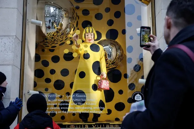 People watch as a lifelike robot of Japanese artist Yayoi Kusama paints spots on the window of the luxury retailer Louis Vuitton store at Place Vendome in Paris, France on January 25, 2023. (Photo by Benoit Tessier/Reuters)