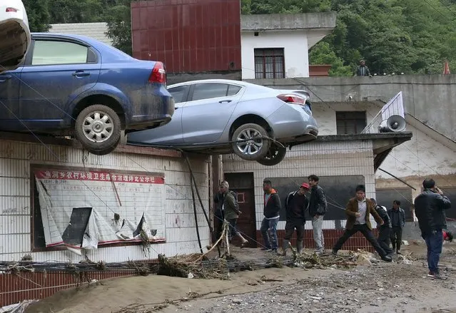 Residents walk on a muddy road next to vehicles pushed up to a wall by floodwater, after heavy rainfall hit Yudong township of Zhenxiong county, Yunnan province May 11, 2015. At least one person was killed and two remain missing after severe rainstorms hit the township on Sunday, local media reported. (Photo by Reuters/China Daily)