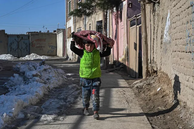 A boy carrying a basket with bread on his head walks along an alley in Kabul on January 26, 2022. (Photo by Mohd Rasfan/AFP Photo)