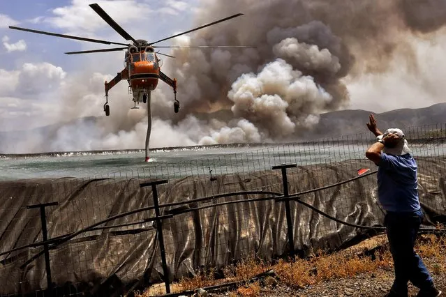 A helicopter is being filled up with water from a tank as a wildfire burns near the village of Spathovouni, near Corinth, Greece on July 23, 2021. (Photo by Vassilis Psomas/Reuters)