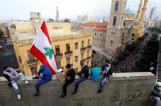 A demonstrator waves the national flag from the balcony of a building during an anti-government rally in Beirut, Lebanon on October 20, 2019. Thousands of people have taken to the streets of Lebanon for a fourth day of protests sparked by tax proposals in the 2020 budget, especially an unexpected plan to impose a fee of 20 cents a day for making WhatsApp calls. (Photo by Mohamed Azakir/Reuters)